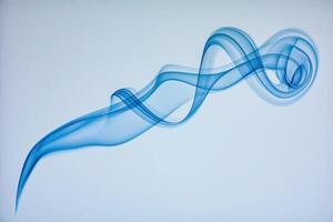 A graceful and ethereal swirl of blue smoke drifts through the air, captivating attention with its fluid motion on a soft, light backdrop. The delicate patterns evoke a sense of calm and tranquility. photo