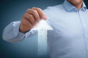 A business professional in a light blue shirt uses their hand to create a digital upward arrow. This action symbolizes growth and progress in a contemporary workspace setting. photo