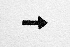 A bold black arrow is drawn on a textured white paper, clearly indicating a rightward direction. The contrast between the black ink and white background highlights the arrows shape and intention. photo