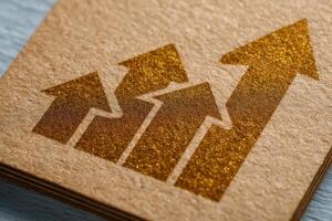 A close-up view displays several upward arrows embossed in gold on a craft paper background, representing growth and progress. The arrangement suggests increasing success over time. photo