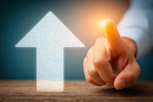 A hand reaches toward a glowing upward arrow, signifying aspiration and improvement. The background is softly lit, enhancing the motivational theme during a business context. photo