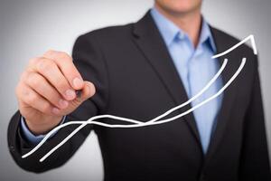 A business professional in a suit is using a marker to illustrate an upward trend on a graph. The setting suggests a corporate or office environment, indicating market growth. photo