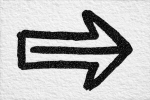 A bold black arrow is drawn on a textured, light background, indicating direction to the right. The arrows simplicity emphasizes clarity and purpose in visual communication. photo