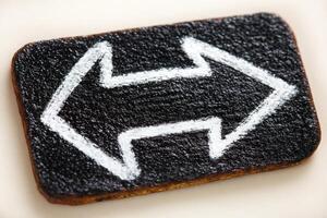 A rectangular sign features a black textured background with bold white arrows pointing left and right. This vibrant design serves as a directional guide, clearly indicating choices. photo