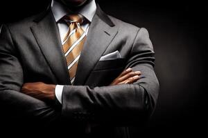 A confident businessman stands with his arms crossed, dressed in a gray suit and striped tie against a dark background. photo