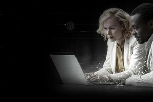 Two professionals are focused on a laptop, analyzing data together in a sleek, modern workspace. Their expressions show concentration and teamwork in a digital environment. photo