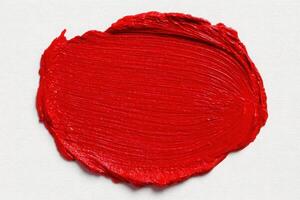 A thick layer of bright red paint is spread on a textured canvas, showcasing its rich color and smooth texture. The paint appears freshly applied, hinting at a creative endeavor in progress. photo