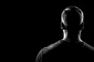 A man stands facing away from the viewer, showcasing a silhouette against a stark black background. photo