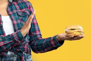Refuse Fast Food. Portrait Of Unhappy African American Woman Holding Burger And Showing Stop Gesture With Palm. Black Lady Rejecting Unhealthy Sandwich, Isolated Over Orange Background, Banner photo