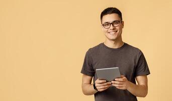 Handsome student blogger works at home on self-isolation. Cheerful young male in glasses with smart watch holds digital tablet and read blog or surfing on internet, isolated on light background photo