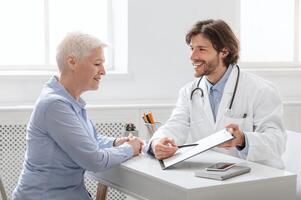 Successful treatment. Cheerful doctor showing good test results to senior patient at hospital, side view photo