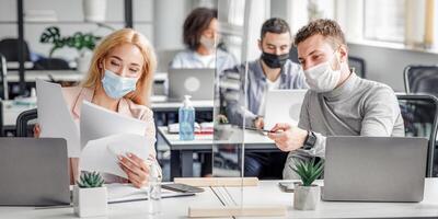 Precautions and social distancing in coronavirus pandemic. Millennial guy and girl in protective masks discussing and working with documents in workplace in office, panorama photo