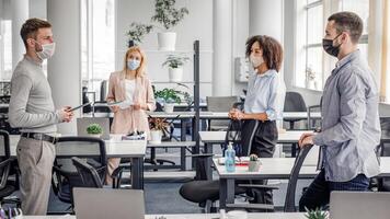 Urgent meeting of colleagues about creative ideas and business plans. Multiracial colleagues in protective masks maintain social distance and discuss new normal at covid-19 in office interior photo