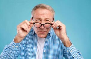 Poor Eyesight. Senior Man Can't See, Squinting Eyes Wearing Glasses Having Problems With Vision, Looking At Camera At Blue Studio. Ophtalmic Issue, Bad Sight In Older Age, Macular Degeneration Concept photo