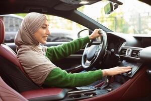 Test Drive Concept. Profile Portrait Of Islamic Lady In Headscarf Driving Car And Turning On Radio Music, Checking Automobile Options, Pushing Button On Functional Panel In Her Luxury Vehicle photo
