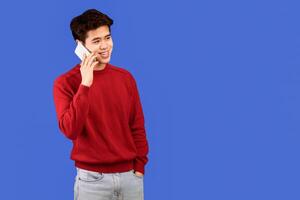 Always In Touch. Portrait of casual smiling asian guy talking on his smartphone, looking aside, standing and posing isolated over blue studio background, banner, copy space. Communication, Phone Call photo