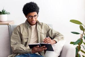 Remote education concept. Black teen college student studying from home during quarantine. African American teenager taking notes for his exam, making homework or getting ready for online class photo