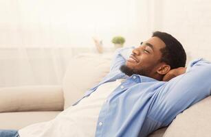 Lazy millennial african american man relaxing at home, holding hands behind head, empty space photo