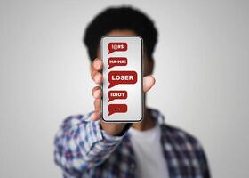 Cyberbullying concept. African American guy showing smartphone with abusive messages on screen, grey background. Collage photo