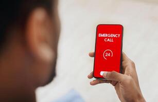 Emergency Call. View over shoulder of man holding phone with 24 hour support line on red screen over blurred background photo