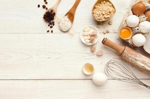 Cooking ingredients background. Border of flour, eggs, raisins, sugar and kitchen utensils on white rustic wood with copy space. Dough preparing and pastry concept, top view photo