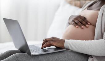 Pregnancy And Technology. Unrecognizable Black Pregnant Lady Using Laptop At Home, Browsing Internet, Shopping Online Or Reading Maternity Blog, Cropped Image, Side View Shot With Free Space, Closeup photo