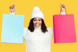 Portrait Of Smiling African American Woman Holding And Showing Two Shopping Bags In Both Hands With Mockup Blank Space For Promotional Text Or Design, Isolated Over Orange Background In Studio, Banner photo