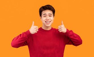 Best Choice, I Like It. Portrait of smiling asian guy showing thumbs up gesture with both hands, approving or recommending something good. Man posing isolated over orange studio background photo