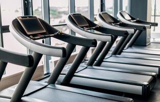 Sport Equipment. Modern Treadmills With Control Panels Standing In A Row At Gym Interior, Closeup Shot Of Training Tools For Running Placed Near Panoramic Windows In Fitness Club Without Visitors photo