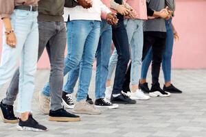 Unrecognizable people holding crossed hands and walking, making strike on the street, side view, panorama. Cropped of multiethnic men and women students activists standing in a row, making live shield photo