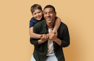 Happy black man have fun posing with cute child preteen boy. Daddy and son embracing and smiling isolated on beige background studio portrait. Fathers Day love family parenthood childhood concept photo