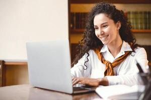 Learning Concept. Portrait of smiling young woman using laptop computer, typing on keyboard and sitting at table. Cheerful lady studying or teaching online at home, doing homework photo