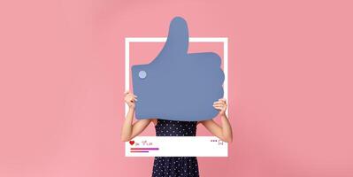 A person is holding a large thumbs up symbol in front of a bright pink background. This vibrant display emphasizes social media engagement, showcasing enthusiasm for content creation. photo
