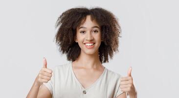 Great result, good choice and cool mood. Happy millennial african american lady student in casual showing thumbs up and looking at camera, isolated on light background, studio shot, free space photo