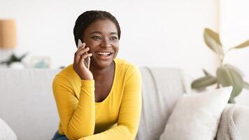Phone Call. Joyful Young African American Woman Talking On Cellphone At Home, Speaking With Friend And Smiling, Having Pleasant Conversation, Enjoying Mobile Communication, Sitting On Sofa, Free Space photo