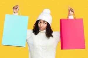 Marketing. Portrait Of Pensive Curious Black Lady Holding And Showing Two Shopping Bags In Both Hands With Mock Up Empty Space For Promotional Text Or Design, Isolated On Orange Studio Background photo