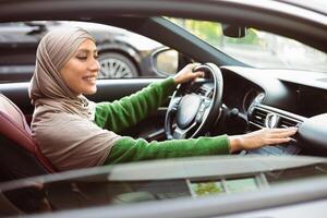 Side View Profile Portrait Of Muslim Woman In Hijab Driving Car And Checking Flow Of Cold Air From Conditioning System, Turning On Radio Music On Functional Panel In Her Luxury Vehicle photo