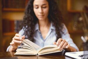 Education And Free Time. Portrait of young woman reading book, sitting at the table at home office, stuying and learning, enjoying weekend. Lifestyle, selective focus, blurred background photo