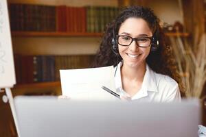 Teleconference And Telecommuting. Portrait of smiling woman in glasses having conference on computer, showing paper document contract to camera, giving presentation or online class to students photo