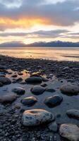 Majestic Sunset Landscape Serene Beach with Rocks, Mountains, and Golden Sky. A breathtaking coastal scene at sunset, showcasing tranquil waters, smooth stones, and a dramatic mountain backdrop. photo