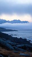 Misty Mountain Majesty A Serene Coastal Landscape. The tranquil fusion of sea, mountains, and fog creates a breathtaking, dramatic scene. Perfect for nature lovers and those seeking serene beauty. photo