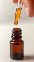 view of a drop of amber liquid falling from a glass pipette into a small brown bottle. The image evokes a sense of precision, care photo