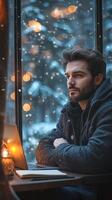 A man sitting at a window looking out at the snow photo