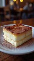A delectable, creamy, layered cake, generously dusted with cocoa powder, sits on a rustic wooden table in a restaurant setting. It photo