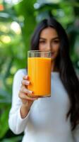 A captivating showcases a womans hand gracefully presenting a tall glass brimming with vibrant, freshly squeezed orange juice. Th photo