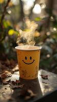 A steaming cup of coffee with a smiley face design, sitting on a table outdoors in the fall. The warm drink and cheerful design ev photo
