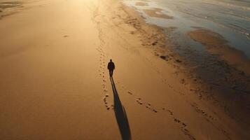 A solitary figure walks along a pristine beach at sunset, leaving footprints in the golden sand. The tranquil ocean waves gently c photo