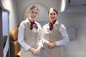 Team of Asian flight attendant posing with smile at middle of the aisle inside aircraft for welcoming passenger on board with seat on background photo