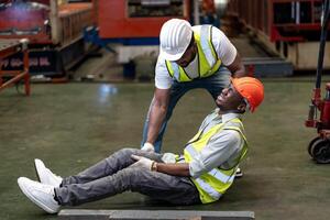 African American factory worker having accident while working in manufacturing site while his colleague is helping for safety workplace and emergency case photo