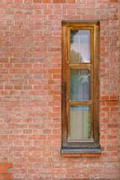 Narrow stylish window in a wooden frame in a red brick wall. Fragment of a residential building. photo